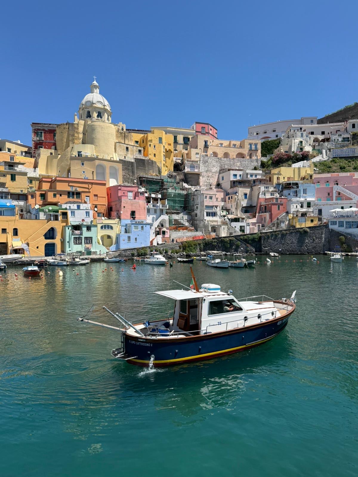 Il Lupo Cattivissimo II, a classic Sciallino 33, at Marina Corricella in Procida beneath the pastel village and church dome